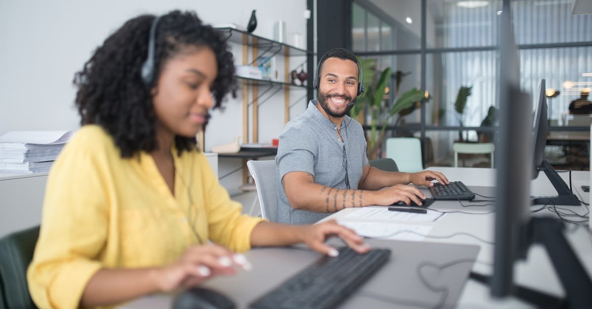 Mulher e homem usando headsets em um escritório, trabalhando em computadores. — Foto: Kampus Production