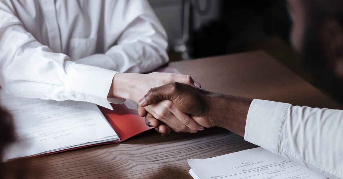 Duas pessoas em uma reunião profissional, apertando mãos sobre documentos em uma mesa. — foto: ron lach