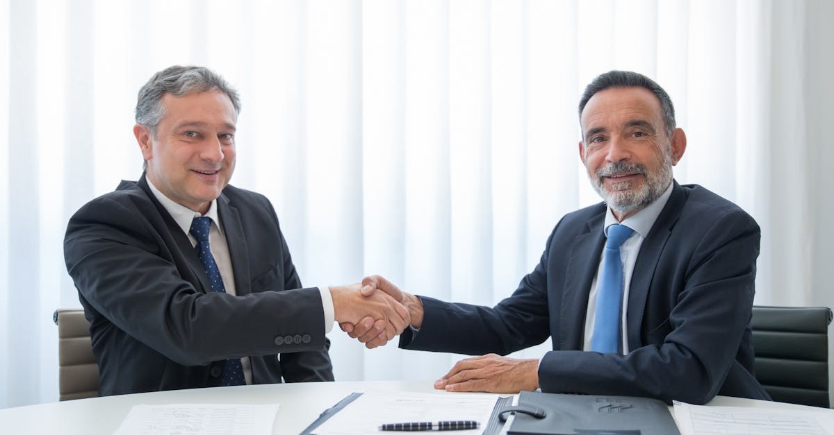 Company formation for foreigners in brazil inline 2 170771 1780839185 Dois homens em terno apertando mãos em uma mesa com documentos e canetas. — foto: kampus production
