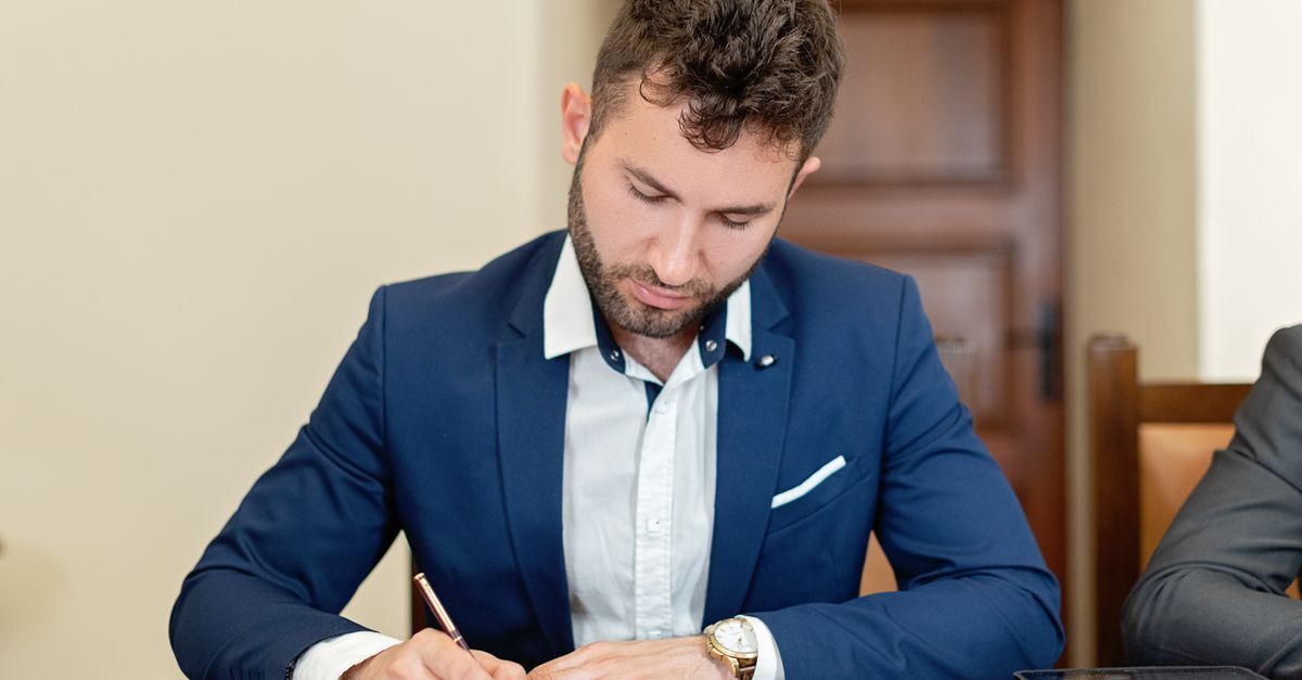 Homem em terno azul escrevendo em um documento em um ambiente de escritório. — foto: mikhail nilov