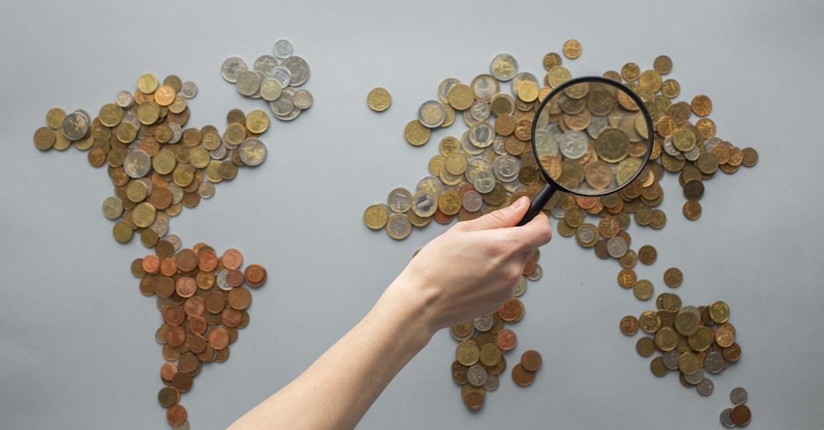 Mão com lupa sobre moedas formando mapa mundial, simbolizando análise financeira global. — Foto: Monstera Production