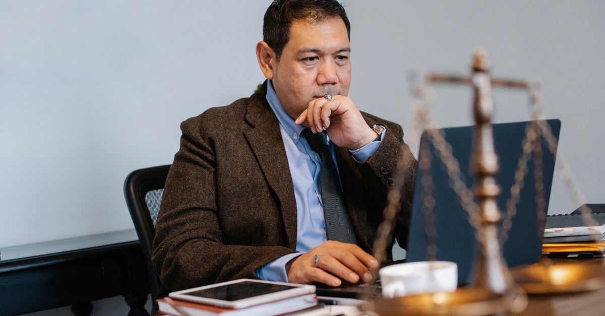 Negativacao indevida inline 2 208753 1781523177 Homem em blazer olhando para a tela de um laptop em um escritório, com balança de justiça e documentos à sua frente. — foto: sora shimazaki