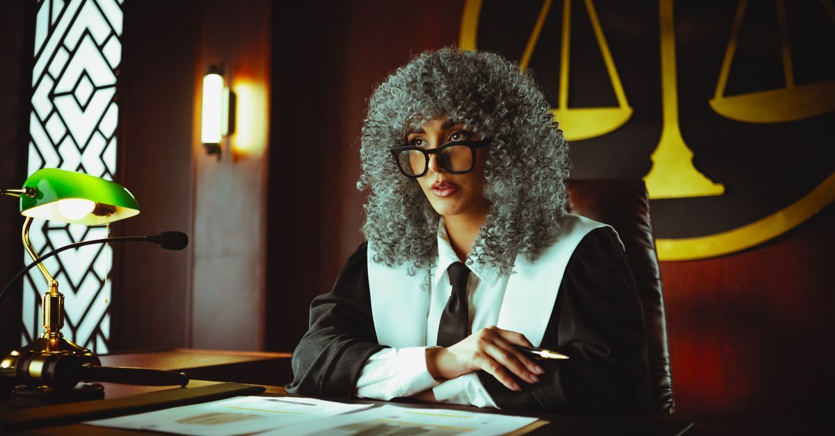 Advogado com peruca e óculos analisando documentos em ambiente de tribunal. — foto: khezez  | خزاز
