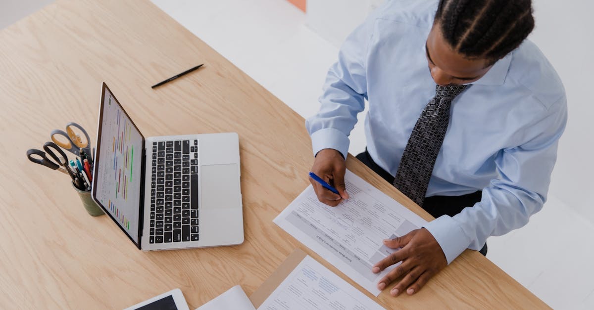 Homem escrevendo em documentos com laptop e tesoura em uma mesa de escritório. — foto: rdne stock project