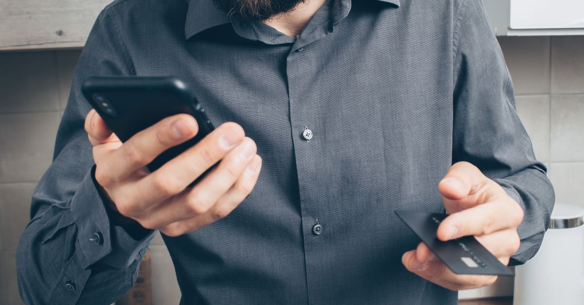 Homem segurando um smartphone e um cartão de crédito em um ambiente doméstico. — foto: mikhail nilov