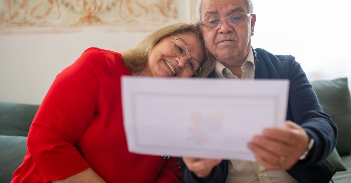 Idosos olhando um documento juntos, em ambiente doméstico.