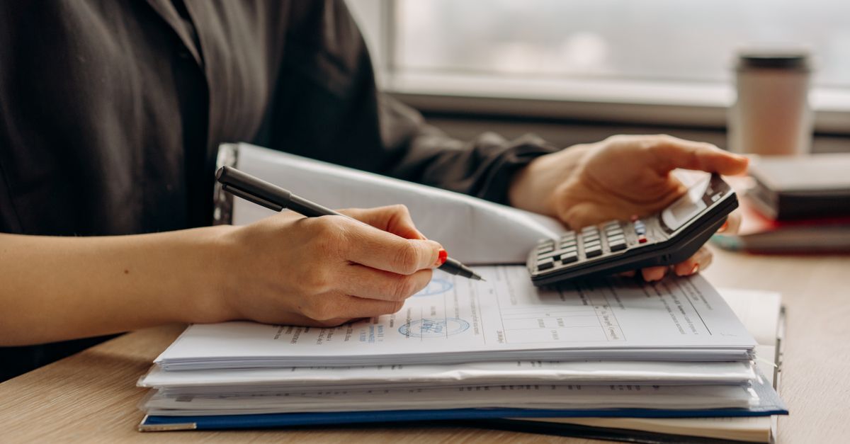 Aposentadoria em 2026 veja as novas idades e regras de pontos inline 1 466333 1785490606 Pessoa escrevendo em documentos com uma calculadora, em um ambiente de trabalho.