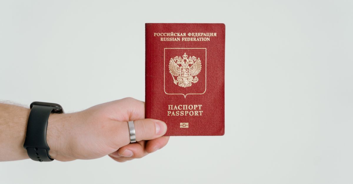Mão segurando um passaporte vermelho com brasão dourado.