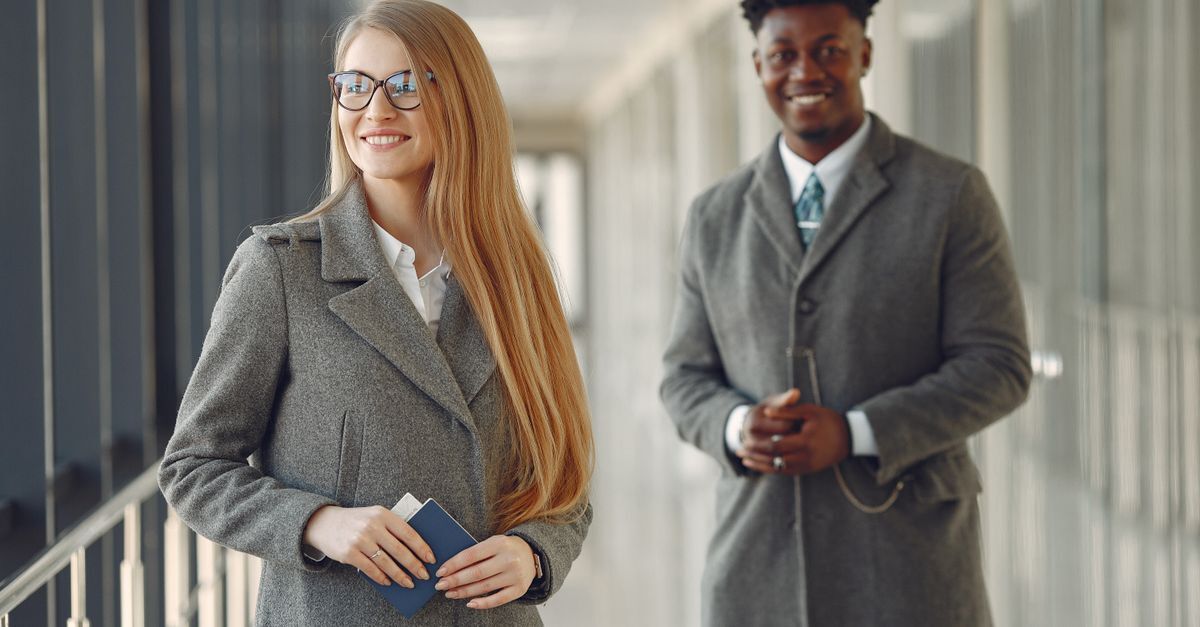 Brazilian residency and future passport pathway for turkish business owners inline 2 379564 1783615170 Mulher de óculos segurando passaporte ao lado de homem de terno em um corredor corporativo.