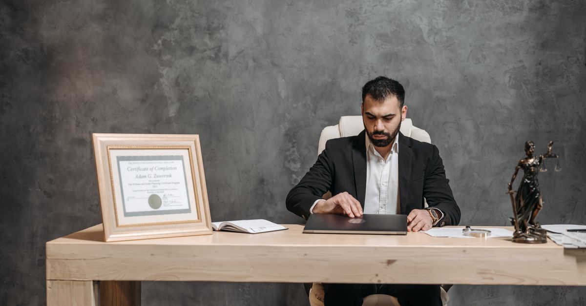 Brazilian residency and passport planning for south african entrepreneurs inline 2 384437 1783701481 Homem de terno sentado em mesa de escritório com notebook, diploma emoldurado e estátua da deusa da justiça.