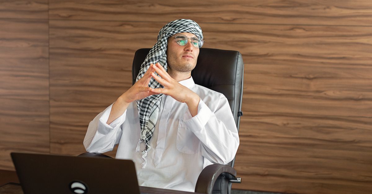 Brazilian saudi investors and families inline 2 370706 1783528766 Homem em traje tradicional sentado em frente a um laptop em um ambiente de escritório.