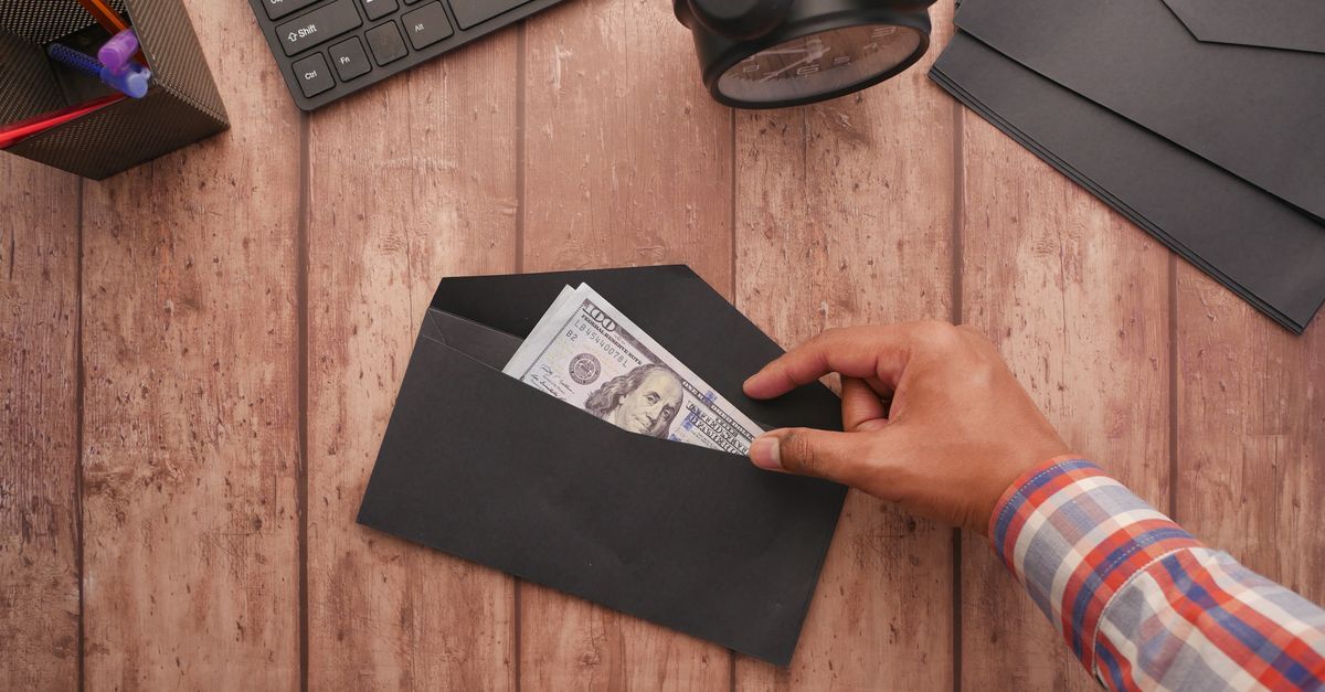Mão retirando dinheiro de um envelope sobre uma mesa de madeira.