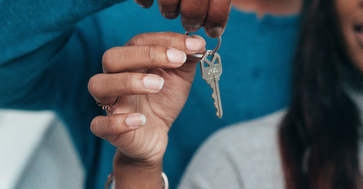 Mão segurando uma chave com outra mão em primeiro plano, sugerindo transação imobiliária.