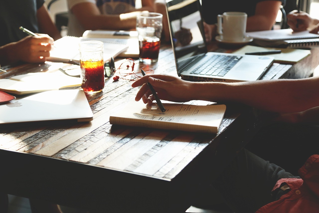 Cartel e crimes contra a ordem economica inline 2 453431 1784650115 Pessoa escrevendo em caderno em reunião de trabalho com notebooks e copos de bebida.