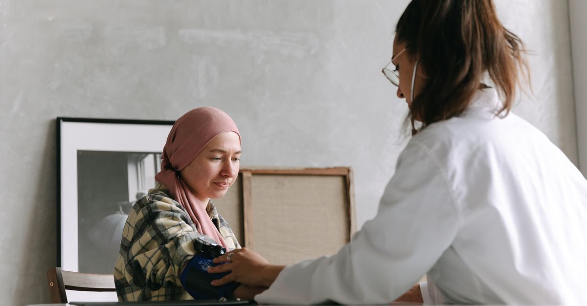 Cid c43 melanoma afastamento auxilio doenca e aposentadoria inline 1 436939 1784311885 Médica de jaleco branco afere a pressão de paciente usando lenço na cabeça em consultório.