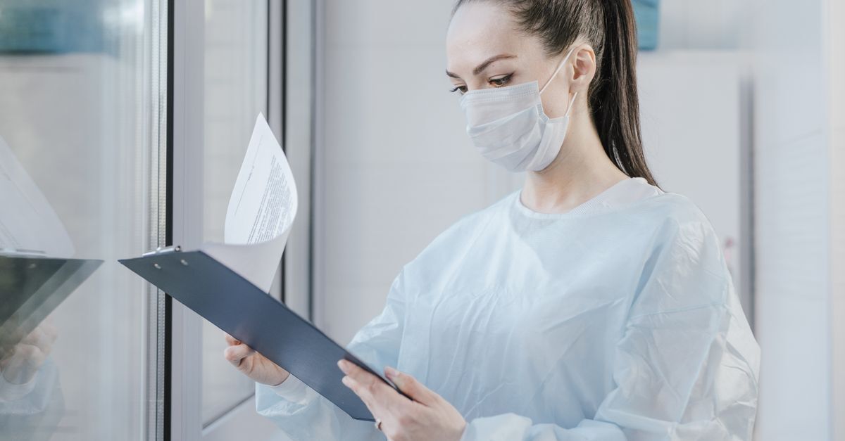 Cid i25 2 pos infarto do miocardio afastamento auxilio doenca e aposentadoria inline 2 360190 1783447660 Profissional de saúde usando máscara e avental cirúrgico analisa documentos em uma prancheta.
