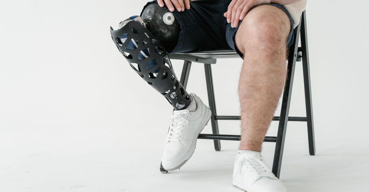 Homem com perna prostética sentando em uma cadeira, usando tênis brancos.