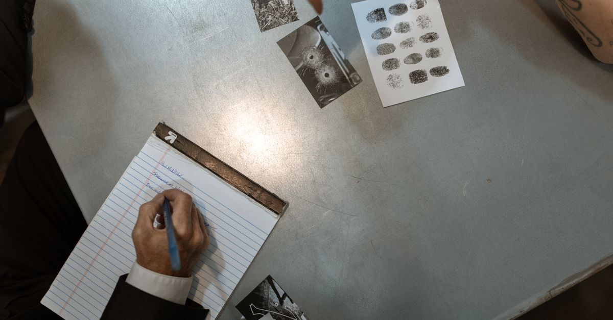 Crimes contra o sistema financeiro inline 1 479272 1785068083 Pessoa escrevendo em um caderno com documentos e fotos de impressões digitais em uma mesa.