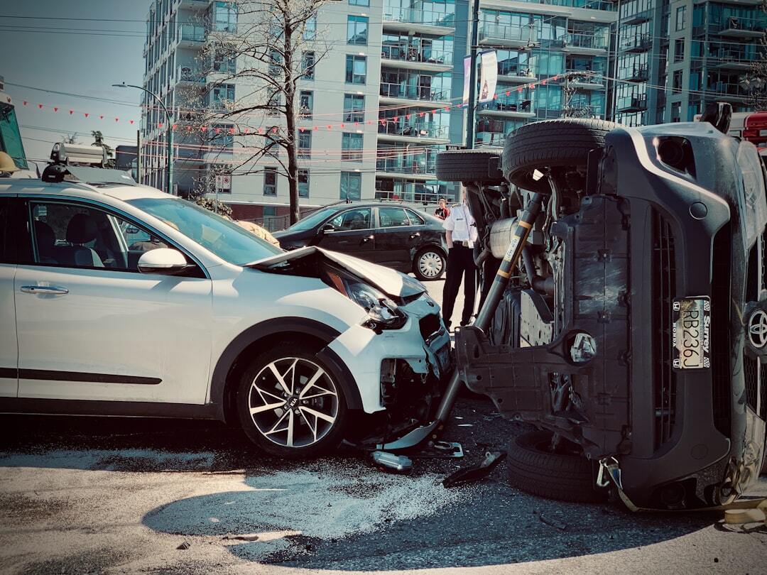 Acidente de trânsito urbano com um carro branco colidido e outro veículo capotado de lado na pista.