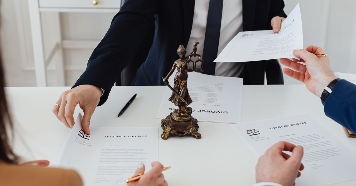 Divorcio inline 1 85547 1785325549 Pessoas assinando documentos em uma mesa com uma estátua de justiça, indicando um processo legal.