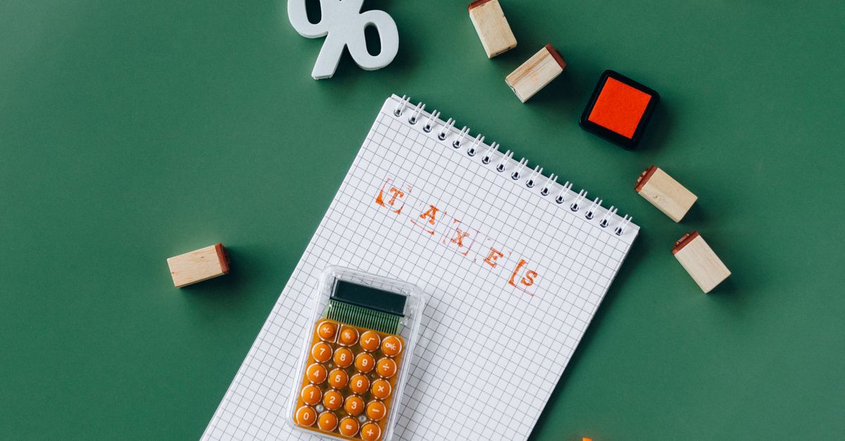 Caderno com a palavra 'impostos' e uma calculadora em uma mesa verde.