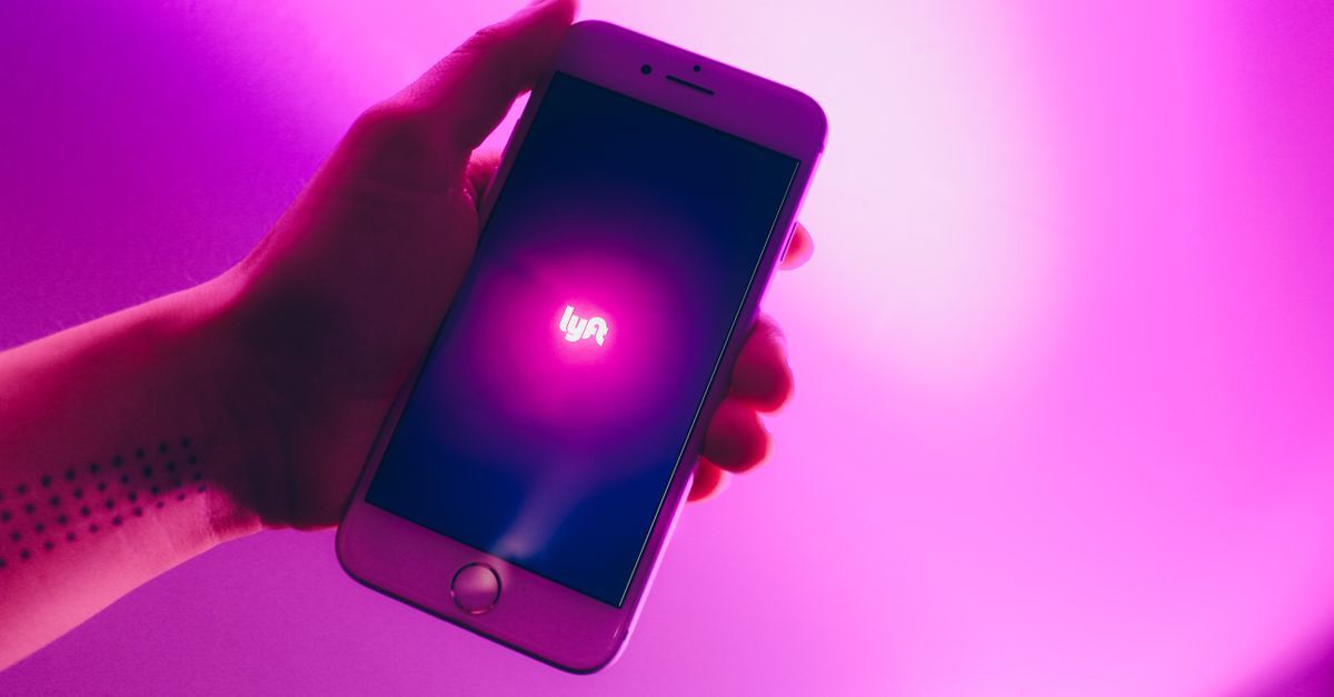 Mão segurando um smartphone com luz rosa no fundo.