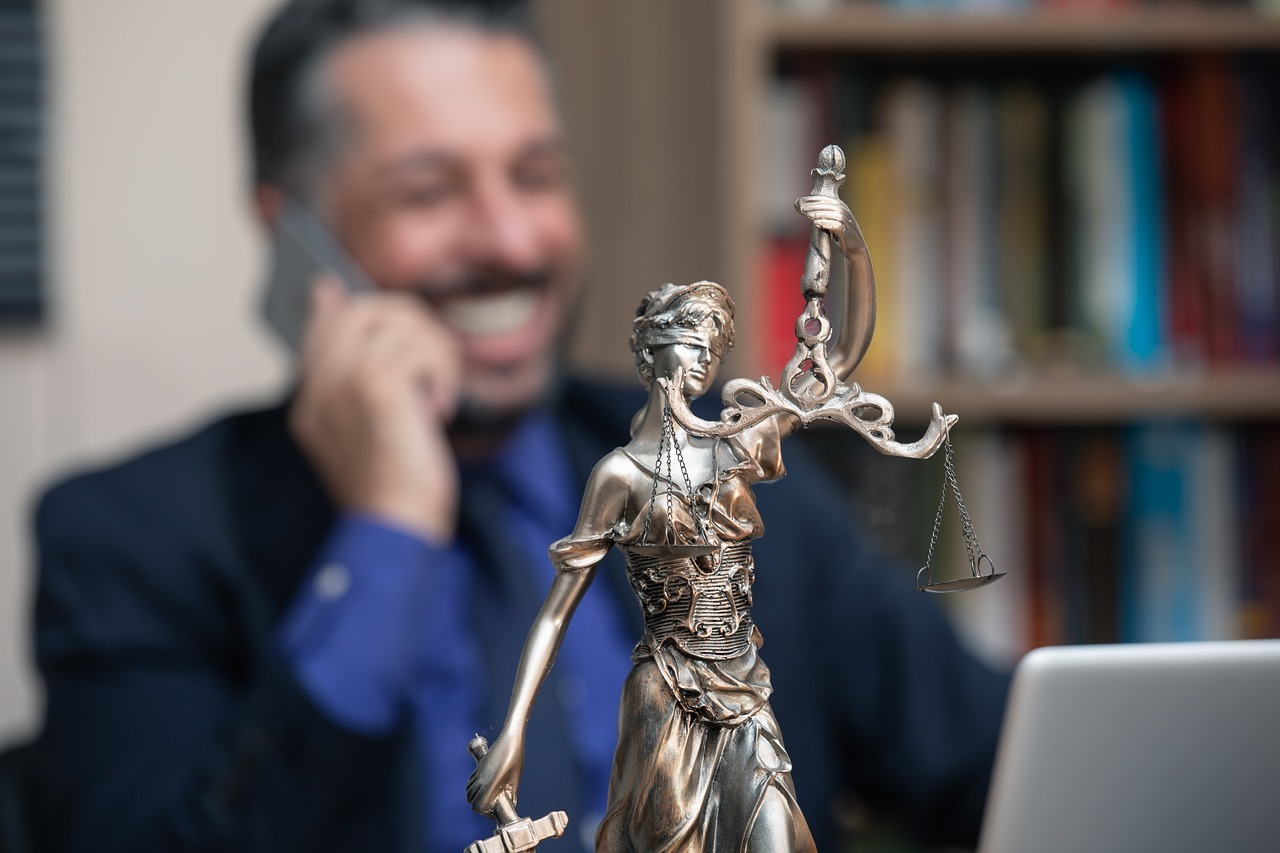 Advogado em conversa telefônica em frente a uma estátua de justiça, em ambiente de escritório.