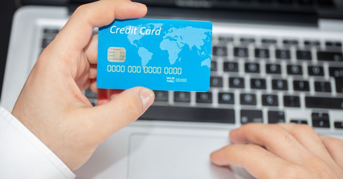 Mão segurando cartão de crédito com fundo de laptop, simbolizando transações digitais e segurança financeira.