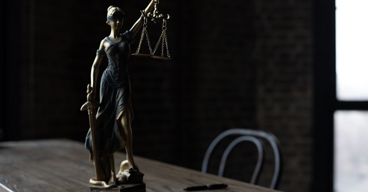 Estátua da deusa da justiça sobre mesa de madeira em escritório de advocacia com fundo escuro.
