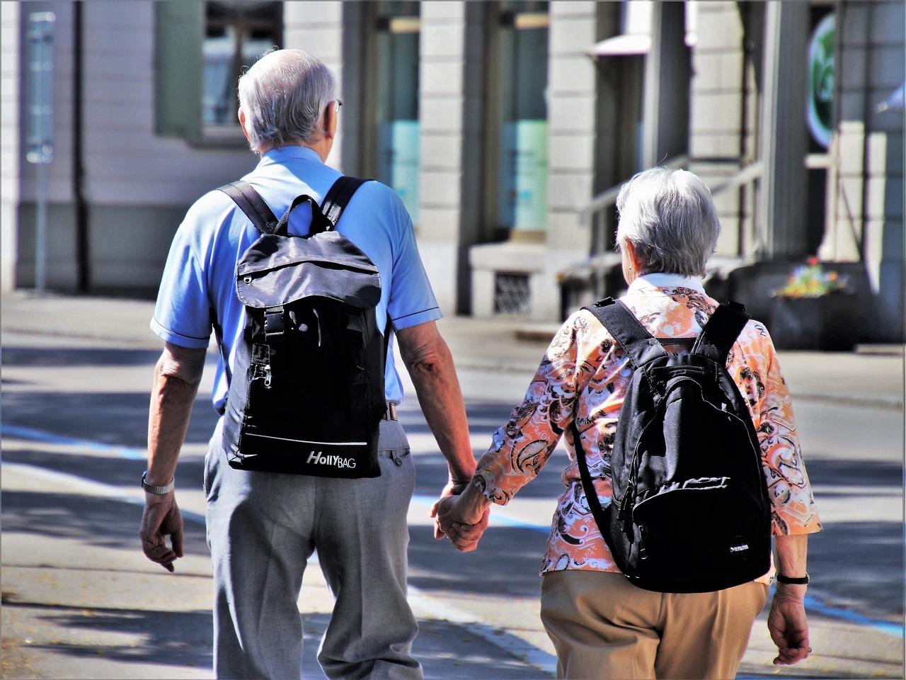 Aposentadoria em 2026 novas idades e regras de transicao inline 1 86582 1785749974 Idosos caminhando na rua, segurando as mãos e com mochilas, em uma cidade.