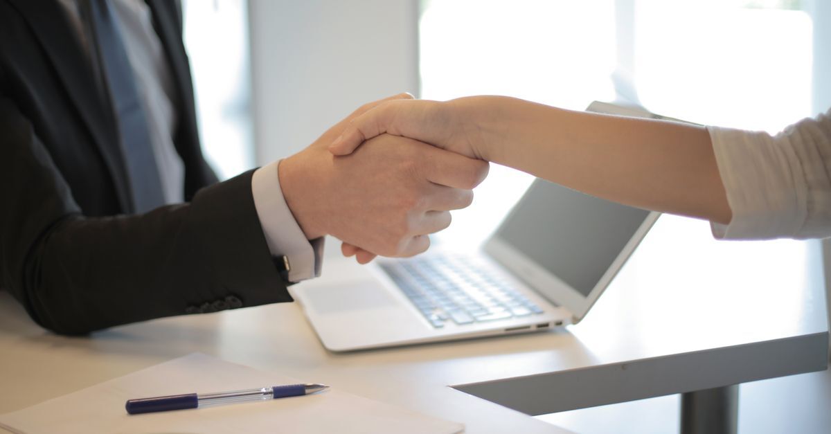Brazil immigration compliance for companies hiring foreign workers inline 1 547077 1785947664 Duas pessoas fazendo um aperto de mão sobre uma mesa com um laptop e uma caneta.
