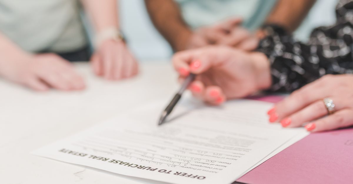 Buying property in brazil as a foreigner inline 1 236200 1786282482 Pessoa assinando um documento em uma mesa, com outras pessoas ao redor.