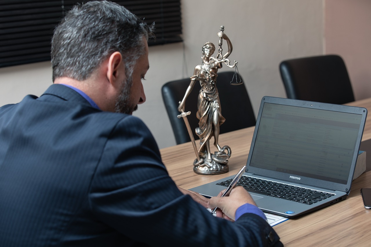 Cadastro nacional de agressores o que muda na protecao a mulher inline 2 524977 1785663500 Homem em blazer escrevendo em frente a um laptop e uma estátua da justiça em uma mesa de escritório.