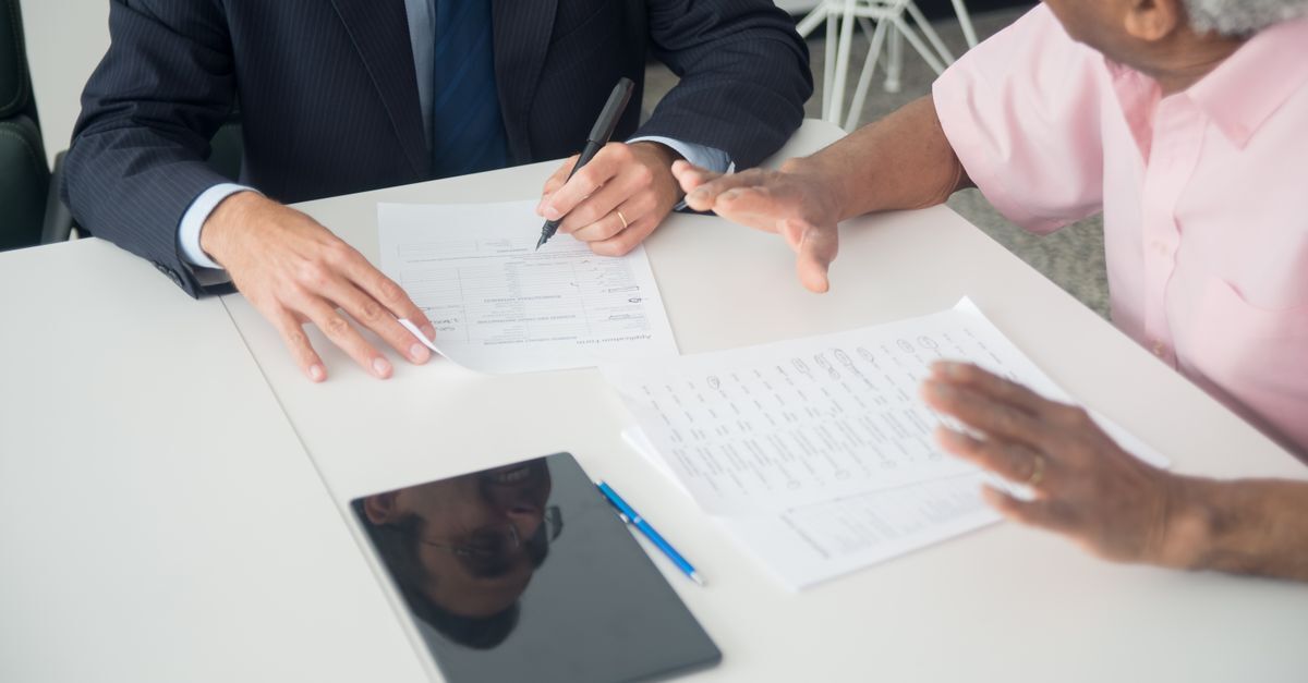 Cid c32 cancer de laringe afastamento auxilio doenca e aposentadoria inline 1 541517 1785866839 Duas pessoas em uma mesa discutindo documentos, uma escrevendo, sugerindo uma consulta ou assinatura de papéis.