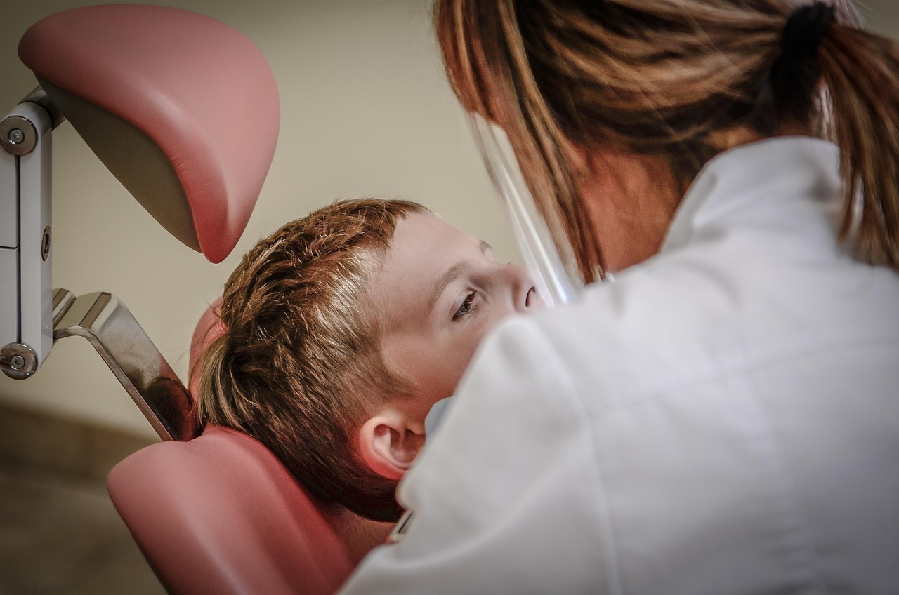 Paciente em uma cadeira odontológica, com uma profissional de saúde em frente.