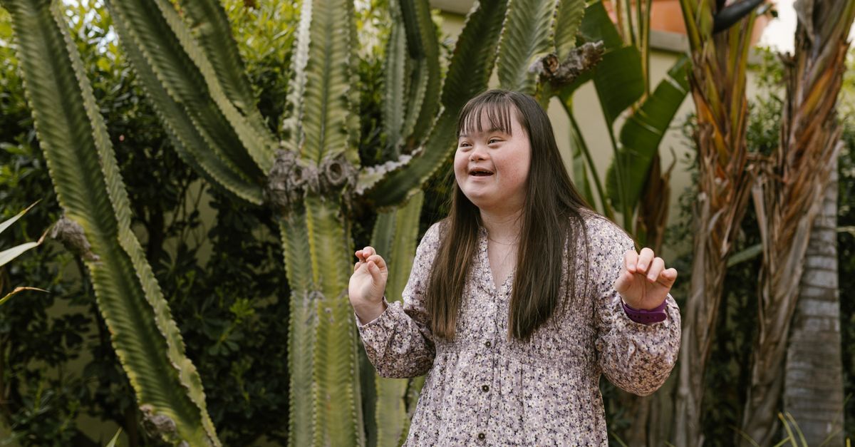 Cid q90 sindrome de down afastamento auxilio doenca e aposentadoria inline 1 577588 1786280738 Mulher com síndrome de down sorrindo em meio a plantas, em um ambiente externo.