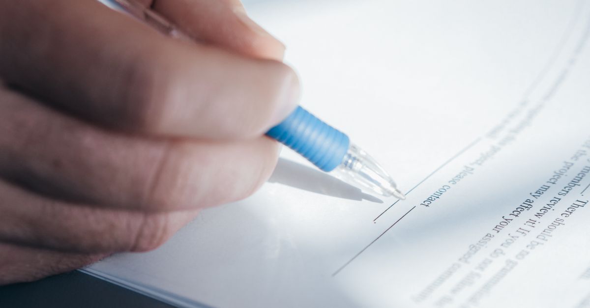 Mão assinando um documento com caneta azul.