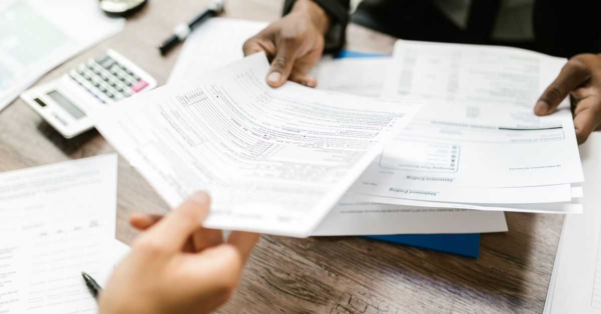 Pessoas revisando documentos em uma mesa de trabalho.