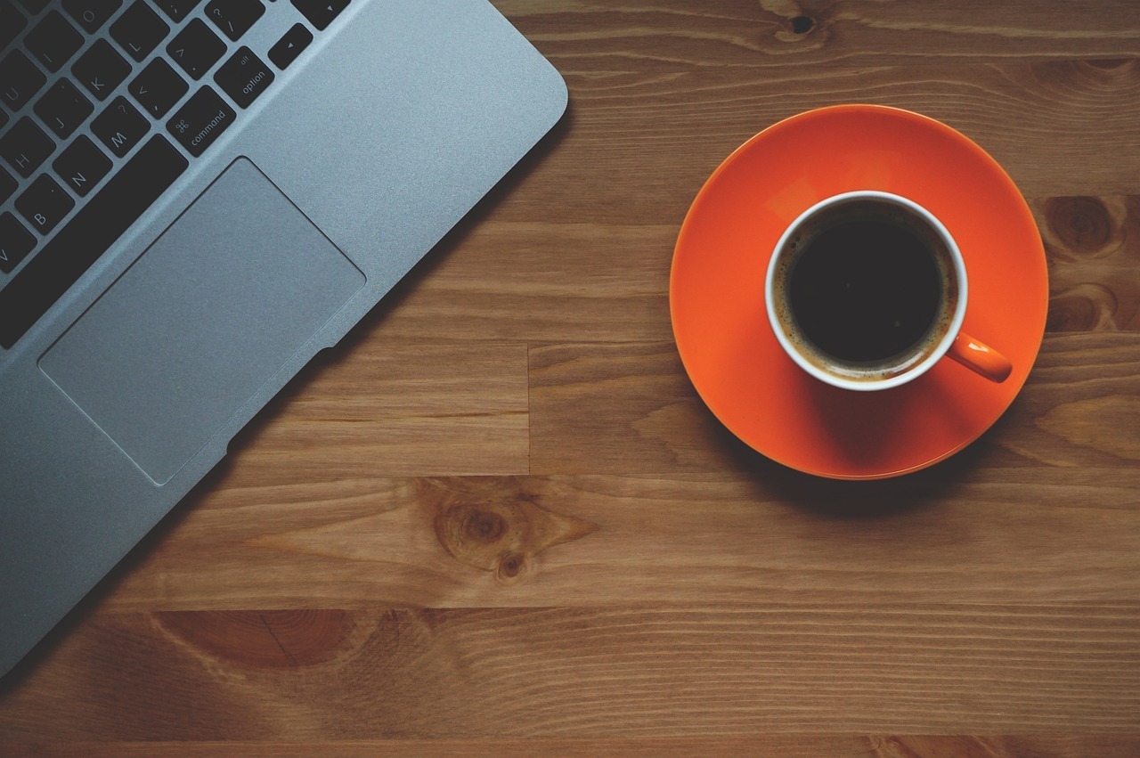 Laptop e xícara de café em uma mesa de madeira, sugerindo uso de dispositivo digital.