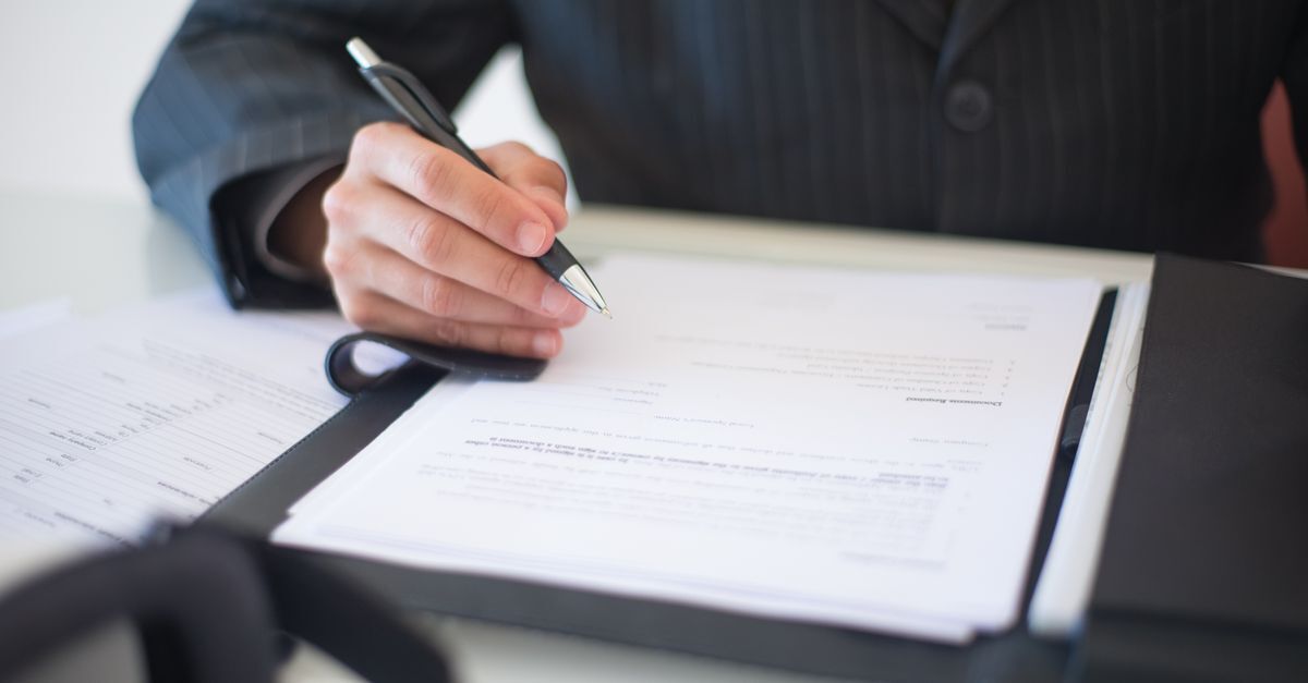 Crimes em licitacoes e contratos inline 2 447504 1787313882 Pessoa escrevendo em documentos em uma mesa, sugerindo a assinatura de contratos ou licitações.