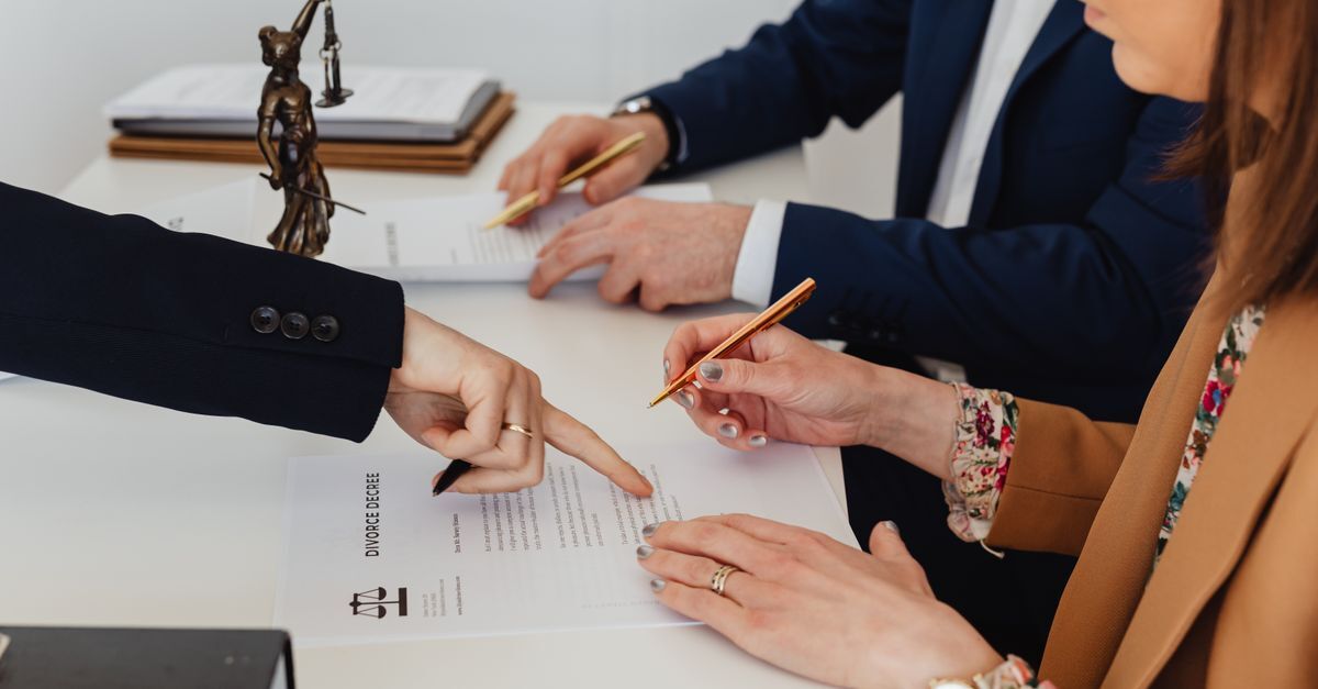 Divorcio inline 1 88197 1786534517 Pessoas assinando documentos em uma mesa, com uma estátua de justiça ao fundo.