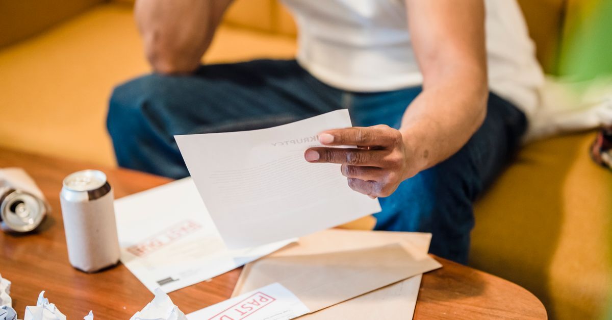 Pessoa segurando um papel sobre uma mesa com outros documentos e uma lata de refrigerante.