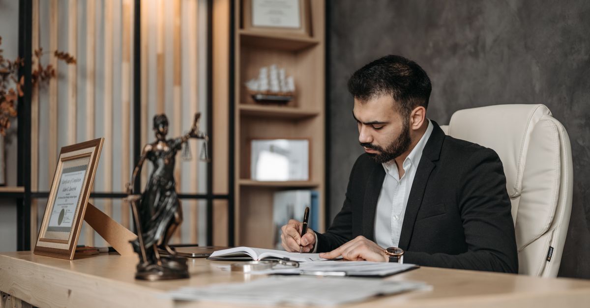 How to find and hire a lawyer in brazil and avoid scams inline 1 611515 1786628105 Homem em uma sala de escritório, escrevendo em documentos, com símbolos jurídicos ao lado.