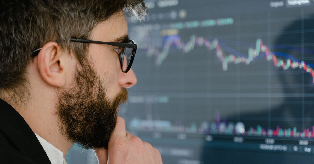 Homem usando óculos e terno, analisando gráficos de mercado em uma tela.