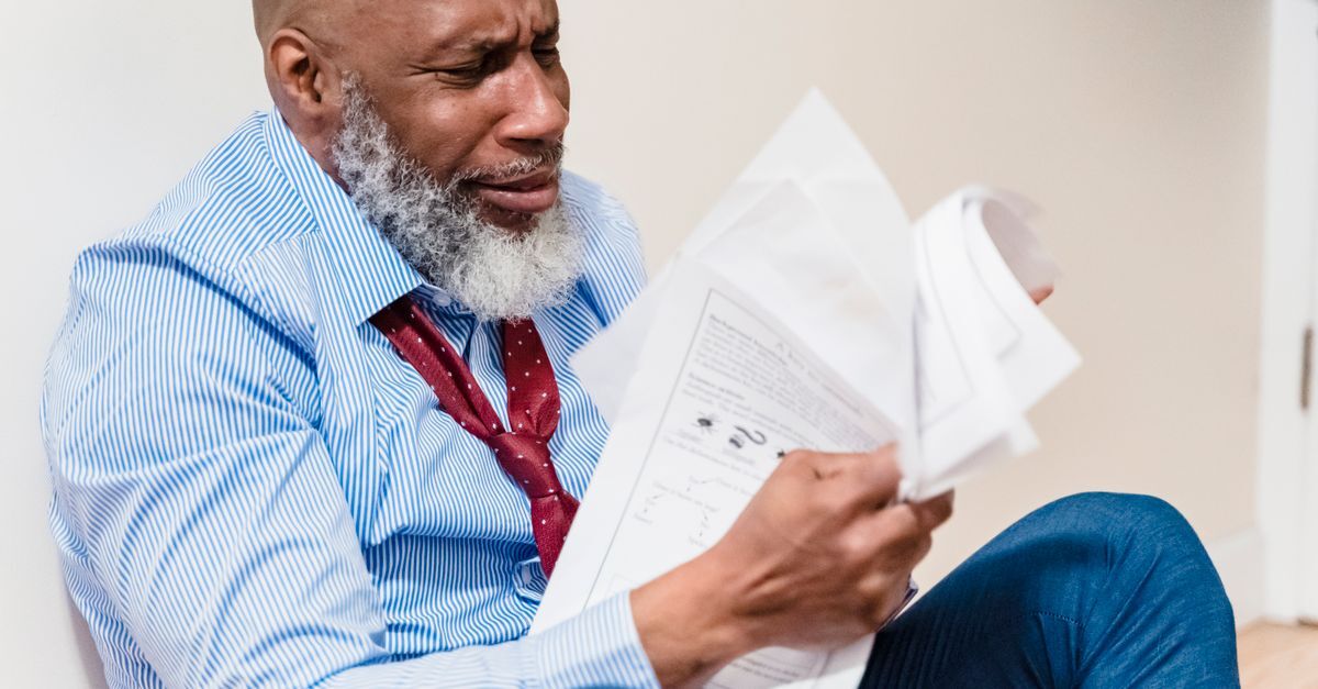 Homem idoso lendo documentos com expressão de preocupação.